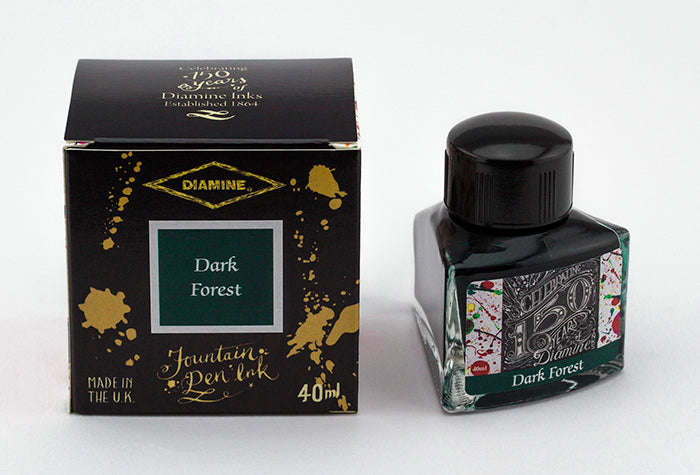 A glass bottle of 40ml Diamine 150th Anniversary Dark Forest fountain pen ink next to packaging box, in front of a white background.