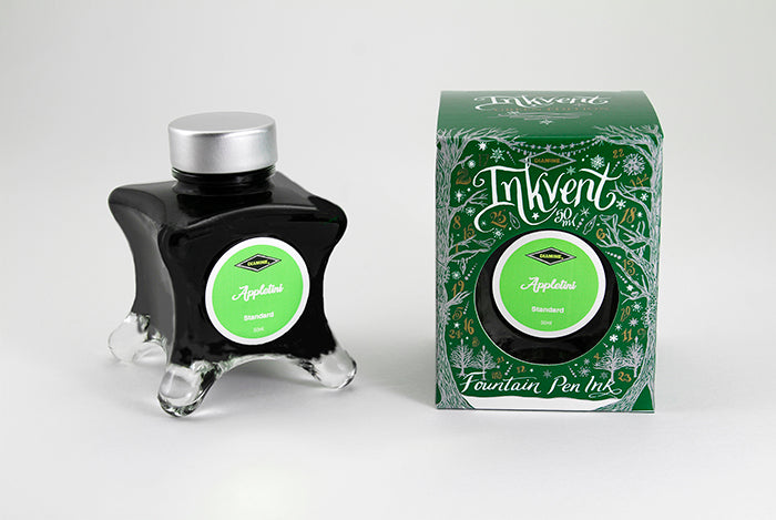 A glass bottle of 50ml Diamine Green Edition Inkvent Appletini fountain pen ink next to packaging box, in front of a white background.
