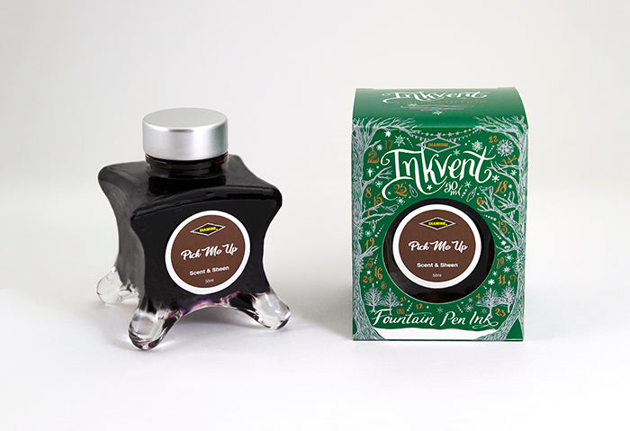 A glass bottle of 50ml Diamine Green Edition Inkvent Pick Me Up scented fountain pen ink next to packaging box, in front of a white background.
