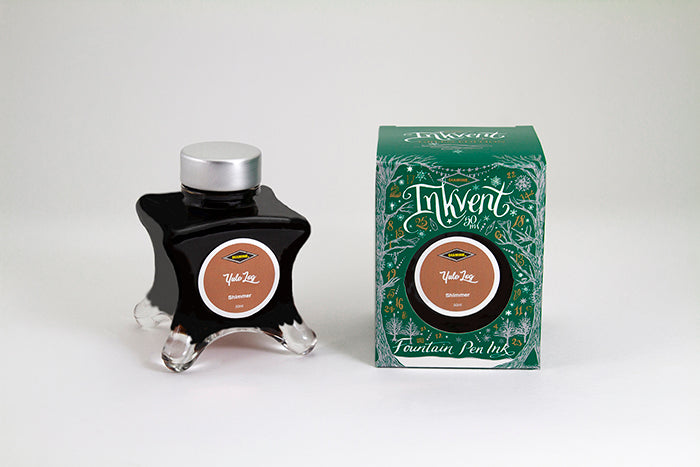 A glass bottle of 50ml Diamine Green Edition Inkvent Yule Log shimmer fountain pen ink next to packaging box, in front of a white background.