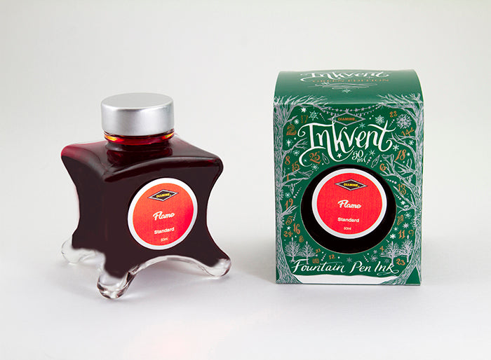 A glass bottle of 50ml Diamine Green Edition Inkvent Flame fountain pen ink next to packaging box, in front of a white background.