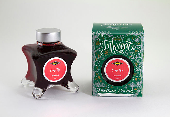 A glass bottle of 50ml Diamine Green Edition Inkvent Cosy Up fountain pen ink next to packaging box, in front of a white background.
