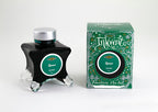 A glass bottle of 50ml Diamine Green Edition Inkvent Spruce scented fountain pen ink next to packaging box, in front of a white background.