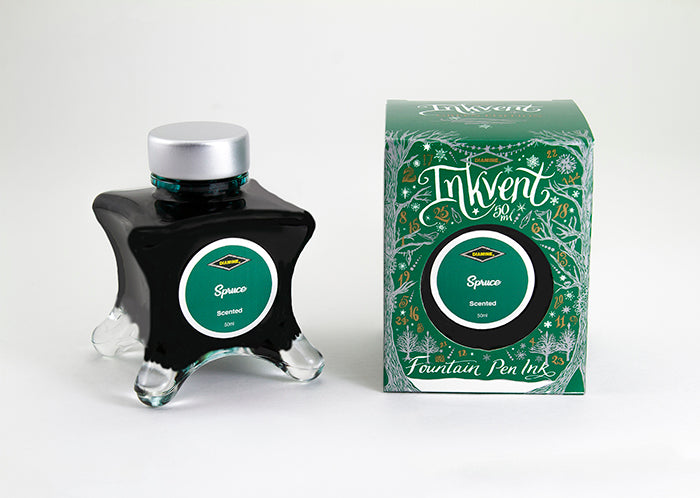A glass bottle of 50ml Diamine Green Edition Inkvent Spruce scented fountain pen ink next to packaging box, in front of a white background.