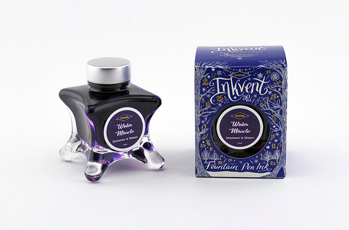 A glass bottle of 50ml Diamine Blue Edition Inkvent Winter Miracle shimmer fountain pen ink next to packaging box, in front of a white background.