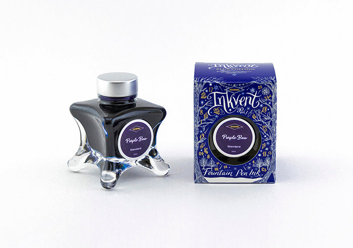 A glass bottle of 50ml Diamine Blue Edition Inkvent Purple Bow shimmer fountain pen ink next to packaging box, in front of a white background.