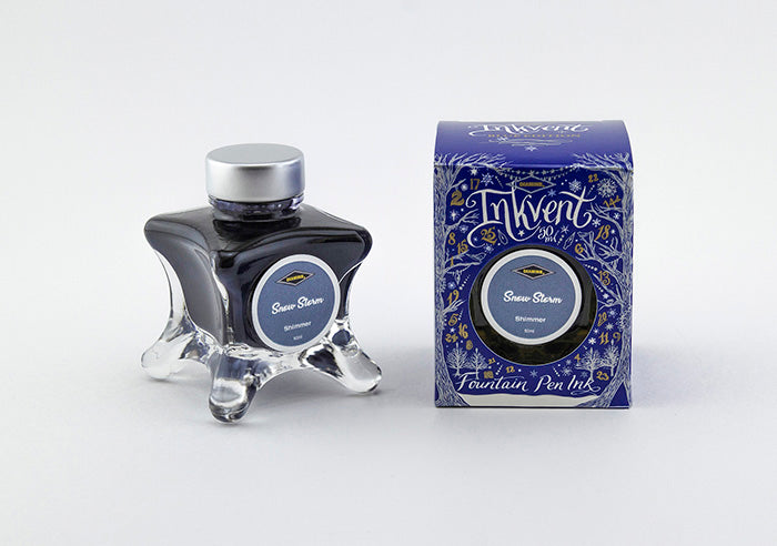 A glass bottle of 50ml Diamine Blue Edition Inkvent Snow Storm shimmer fountain pen ink next to packaging box, in front of a white background.
