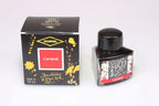 A glass bottle of 40ml Diamine 150th Anniversary Carnival fountain pen ink next to packaging box, in front of a white background.
