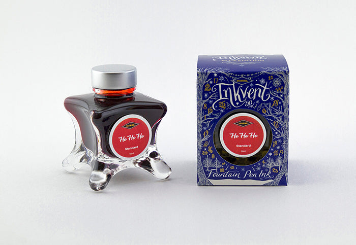 A glass bottle of 50ml Diamine Blue Edition Inkvent Ho Ho Ho fountain pen ink next to packaging box, in front of a white background.