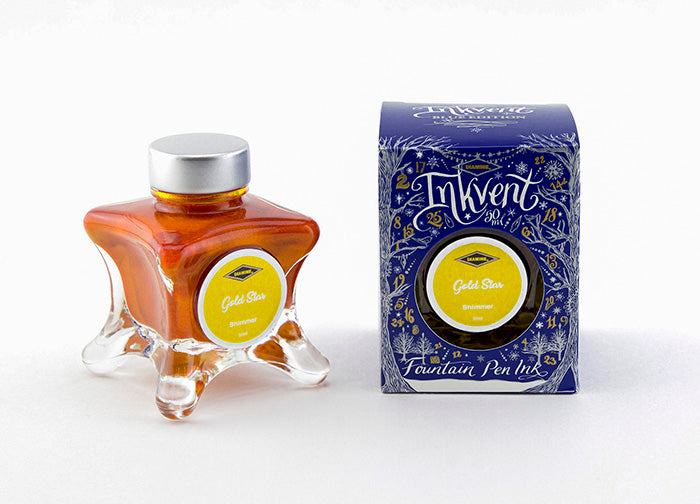 A glass bottle of 50ml Diamine Blue Edition Inkvent Gold Star shimmer fountain pen ink next to packaging box, in front of a white background.