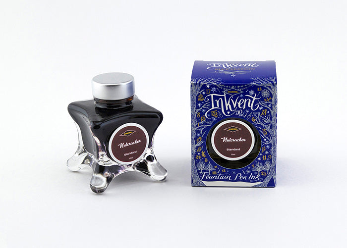 A glass bottle of 50ml Diamine Blue Edition Inkvent Nutcracker fountain pen ink next to packaging box, in front of a white background.